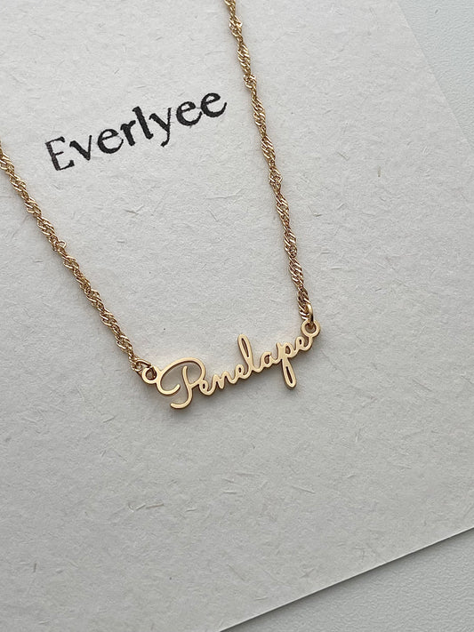 close up picture of golden Penelope name necklace with calligraphy font and Singaporean chain